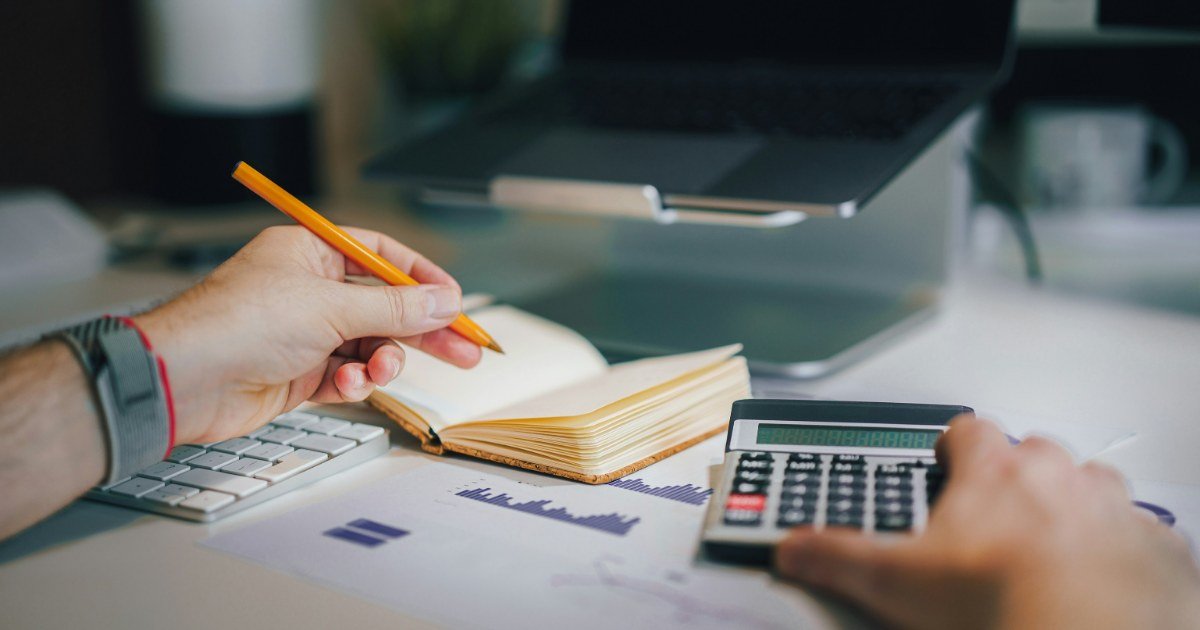 Mesa com calculadora, caderno com contas feitas à mão e um relógio